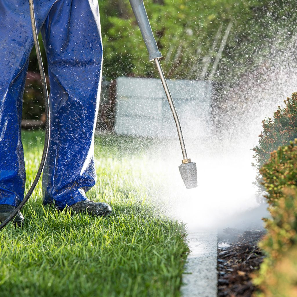 a technician powerwashing the siding of a garden